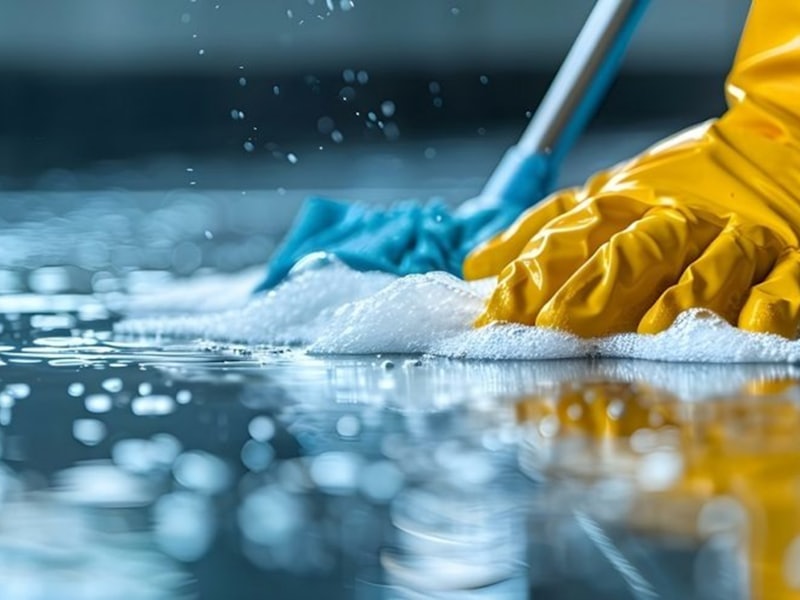 A cleaner in gloves working across a hard floor