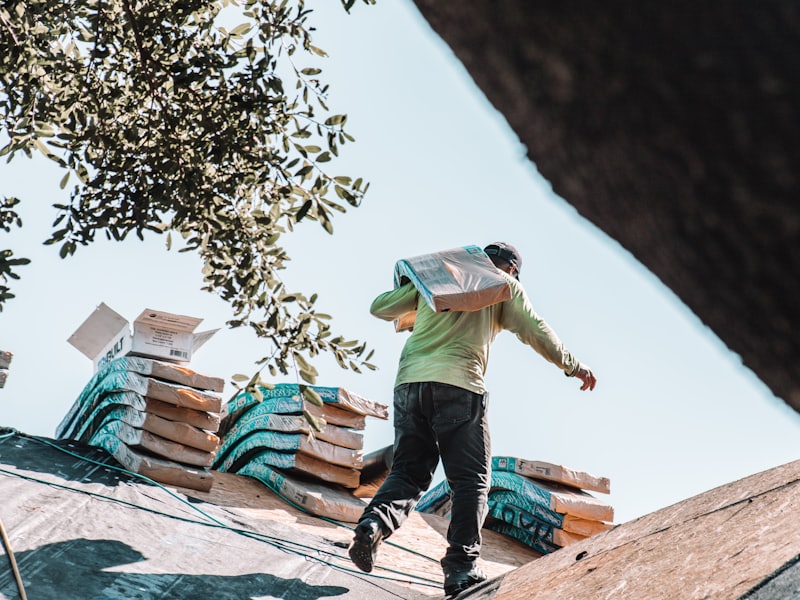 A roofer carrying a bundle of shingles across a residential roof